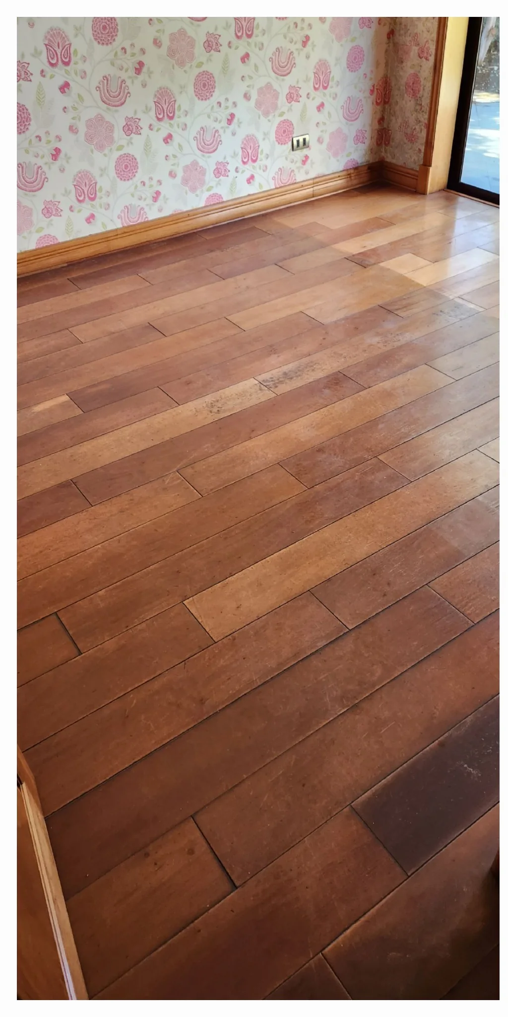 Piso de madera en sala con marcas oscuras junto al muro