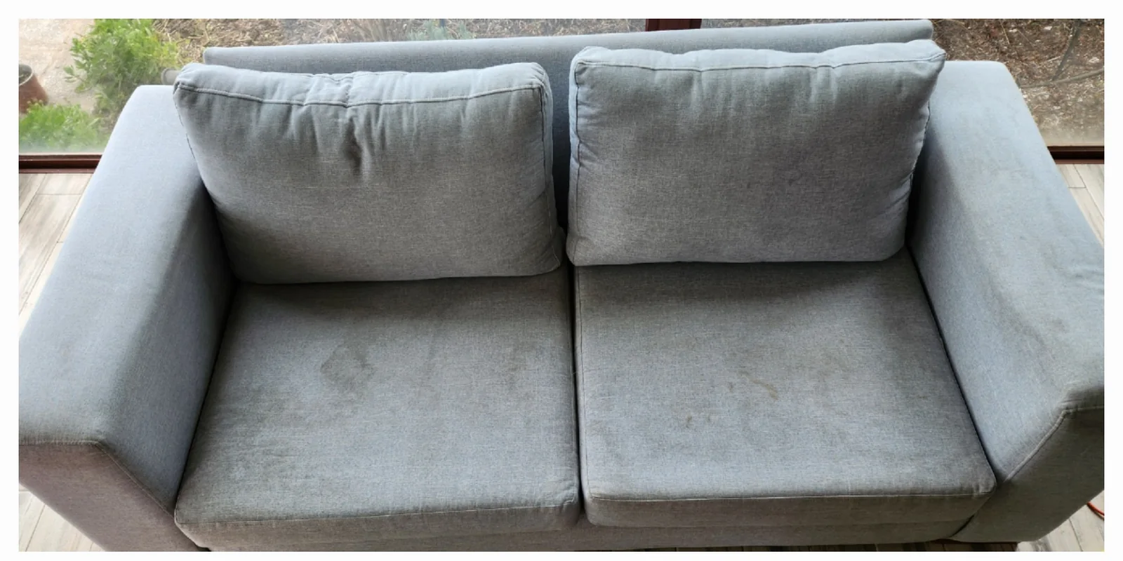 Sillón gris de dos cuerpos con marcas visibles en los asientos antes del lavado