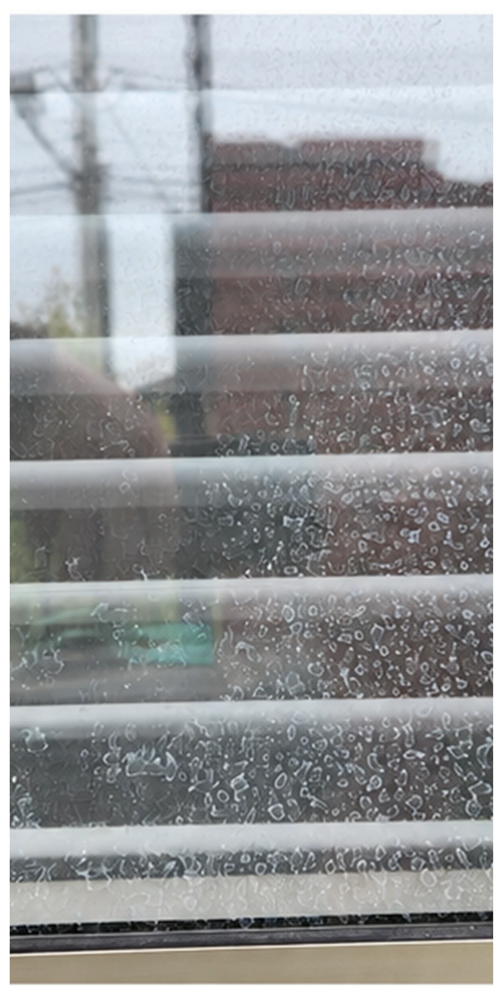Ventana con persiana horizontal y numerosas marcas de agua visibles en el vidrio